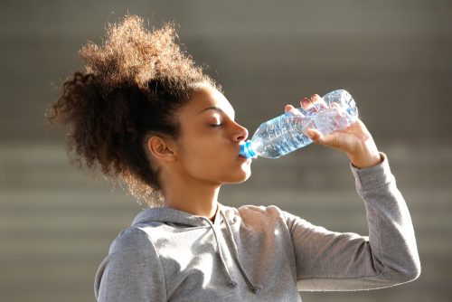 woman in sweatshirt drinking water to prevent constipation