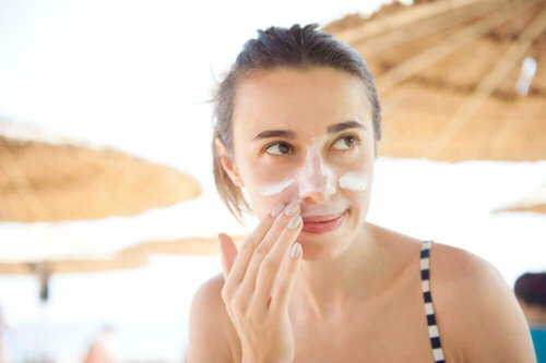 A woman putting on sunblock so she doesn't get a black line on her nail.