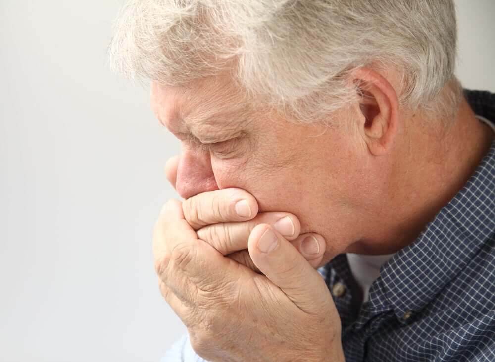 An older man covering his mouth with his hands, looking nauseous.