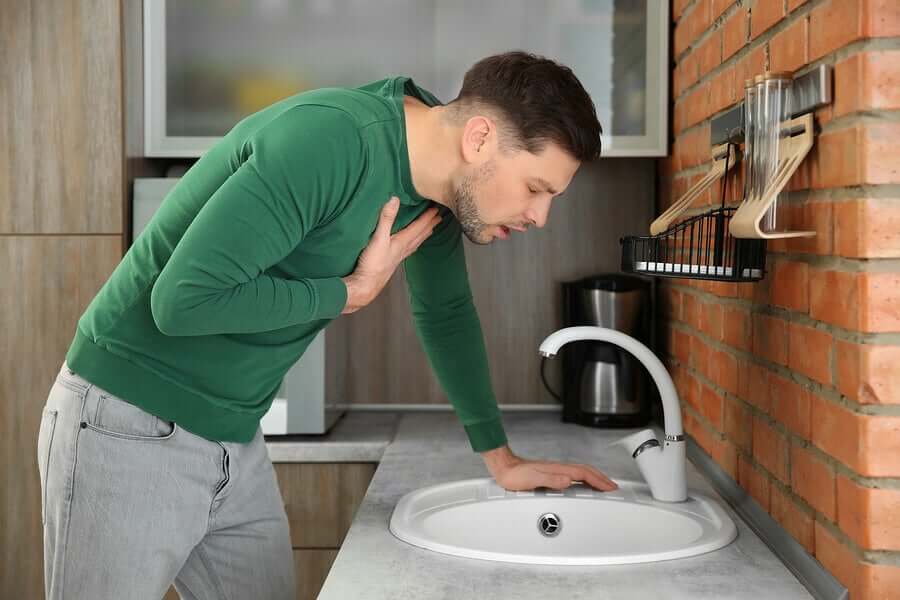 A man leaning over a sink, feeling nauseous.