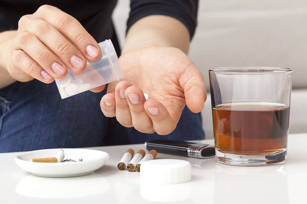 Een persoon drinkt alcohol, rookt, en slikt pillen