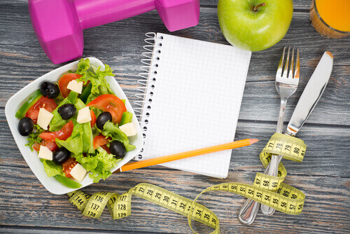 a salad, tape measure, silverware, and a notebook to represent nutrition advice