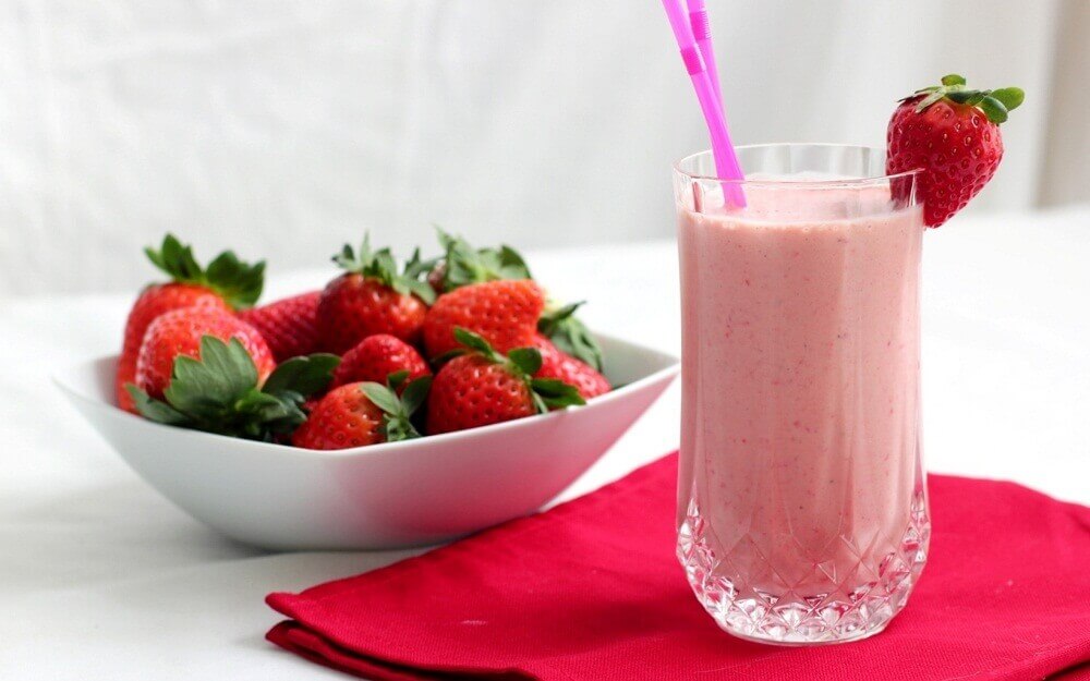 A smoothies and a bowl of strawberries.