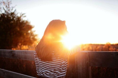 woman looking into the distance standing at a bridge; with the sunset in front of her