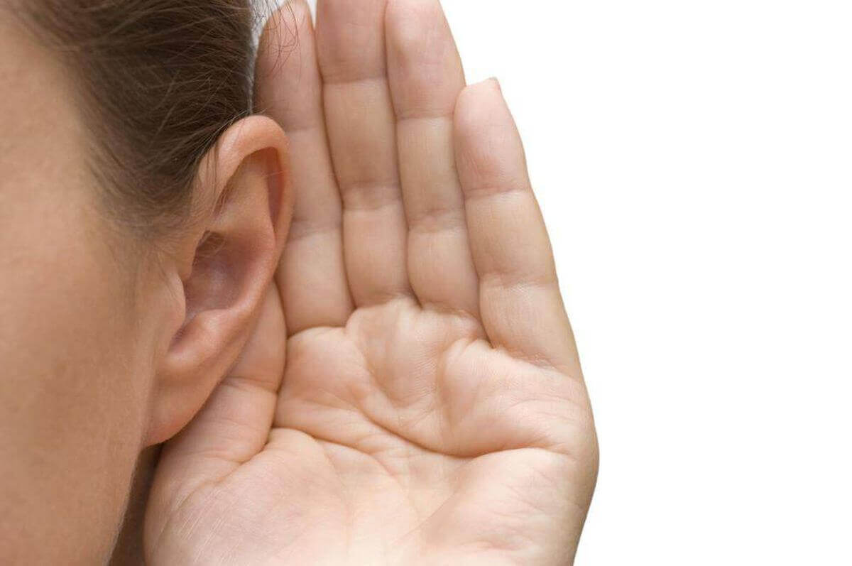 A woman trying to listen with her hand behind her ear.