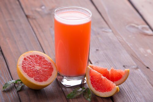 This is a glass of grapefruit juice beside sliced grapefruits.