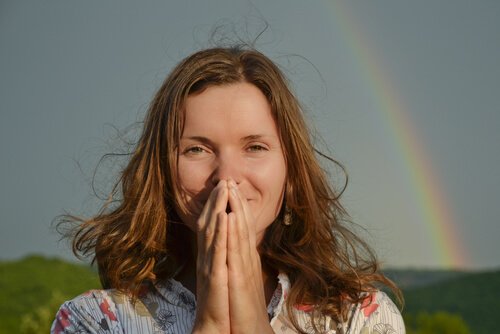 A woman praying in front of a rainbow.