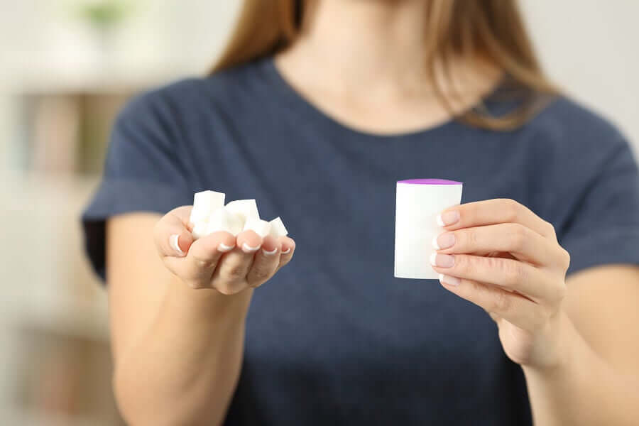 A woman holding sugar cubes and a packet of artificial sweetener in her hands.