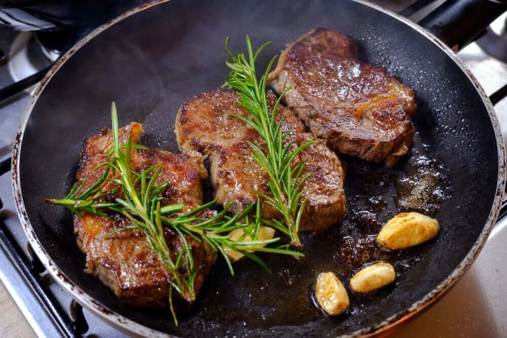 Beef, rosemary, and garlic cooked in a skillet.