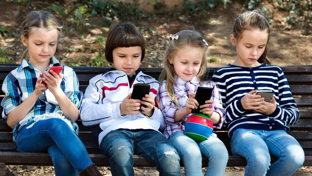 Four children on a bench on their phones