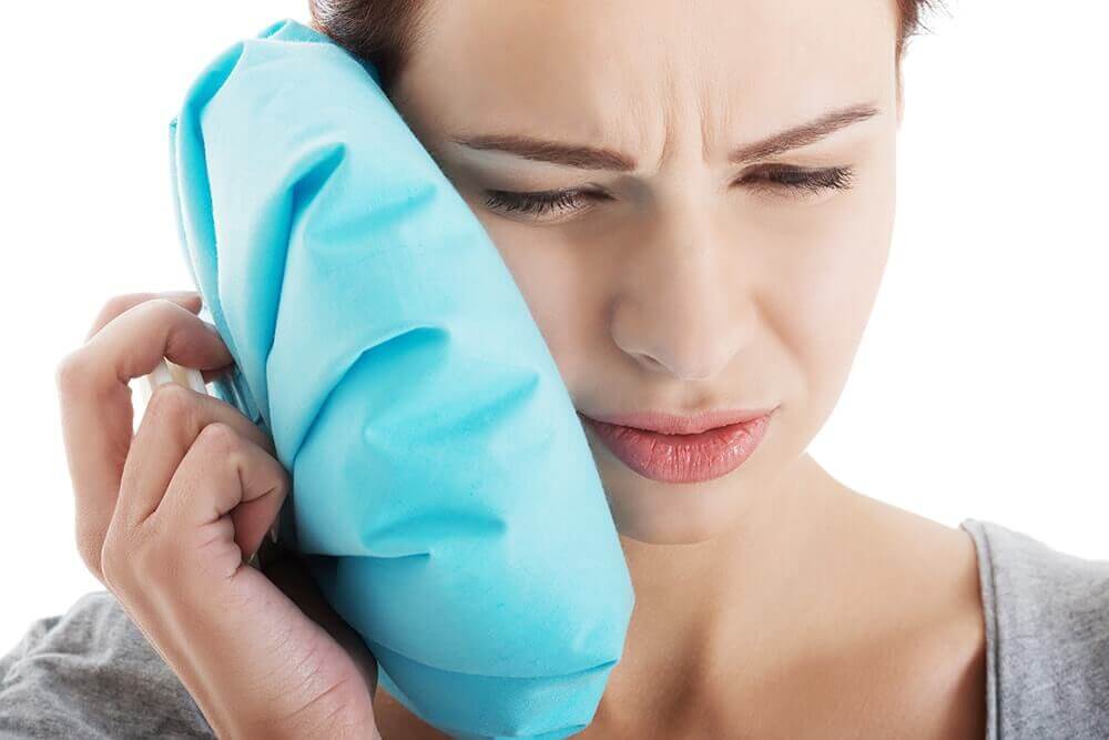 A woman applying a compress to her ear.