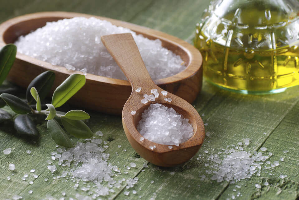 A bowl of sea salt next to a bottle of wheat germ oil