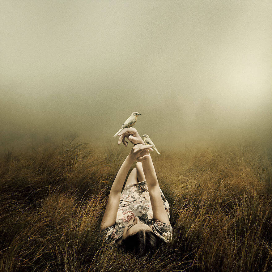 Woman lying in a field playing with birds
