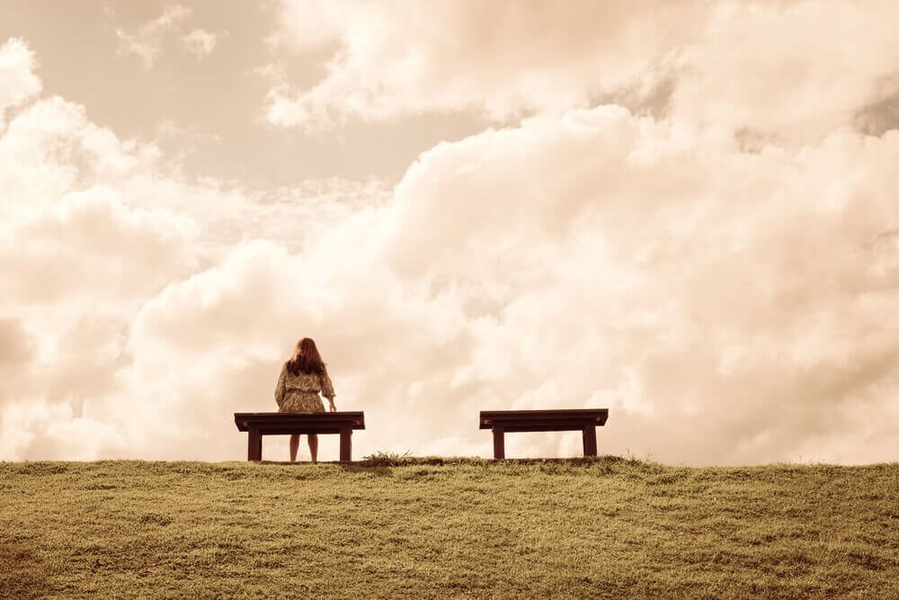 A woman sitting alone on a bench on a hill.