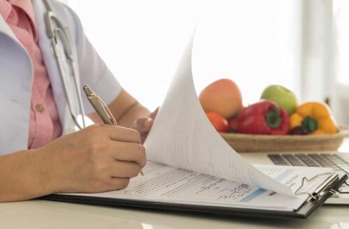 woman writing notes sitting in a white lab coat with peppers and other fruits behind her