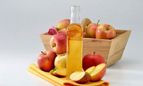 A bottle of apple cider vinegar with some apples