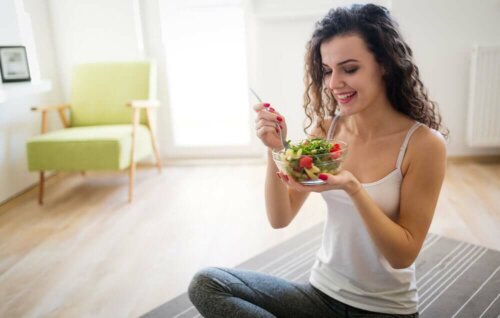 A woman laughing alone with salad.