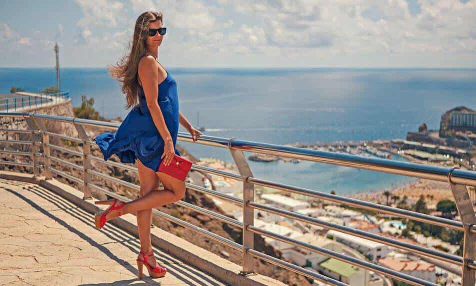 A woman looking over the ocean with heels.