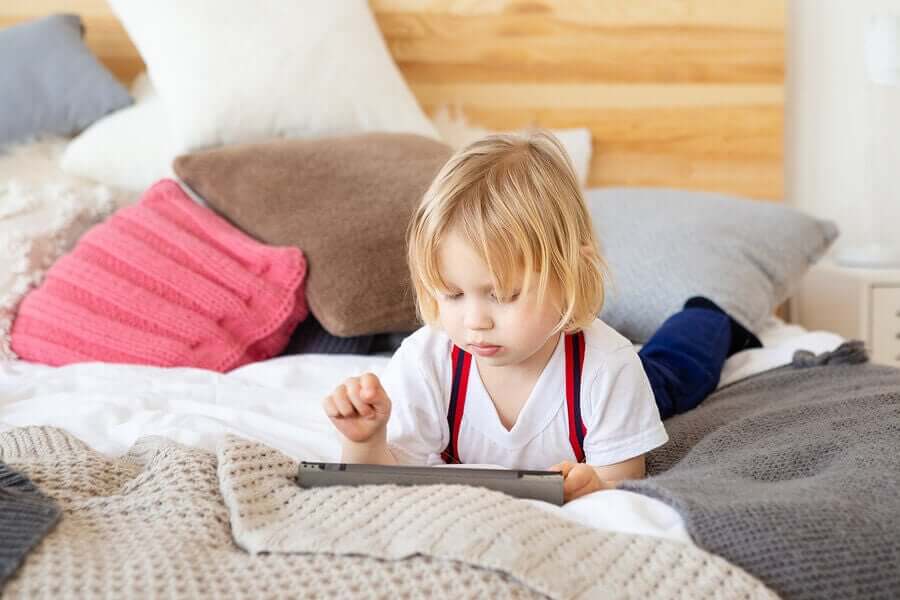 A child looking at a tablet on a bed.