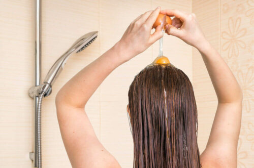 A woman cracking an egg on her hair which helps strengthen fine hair.