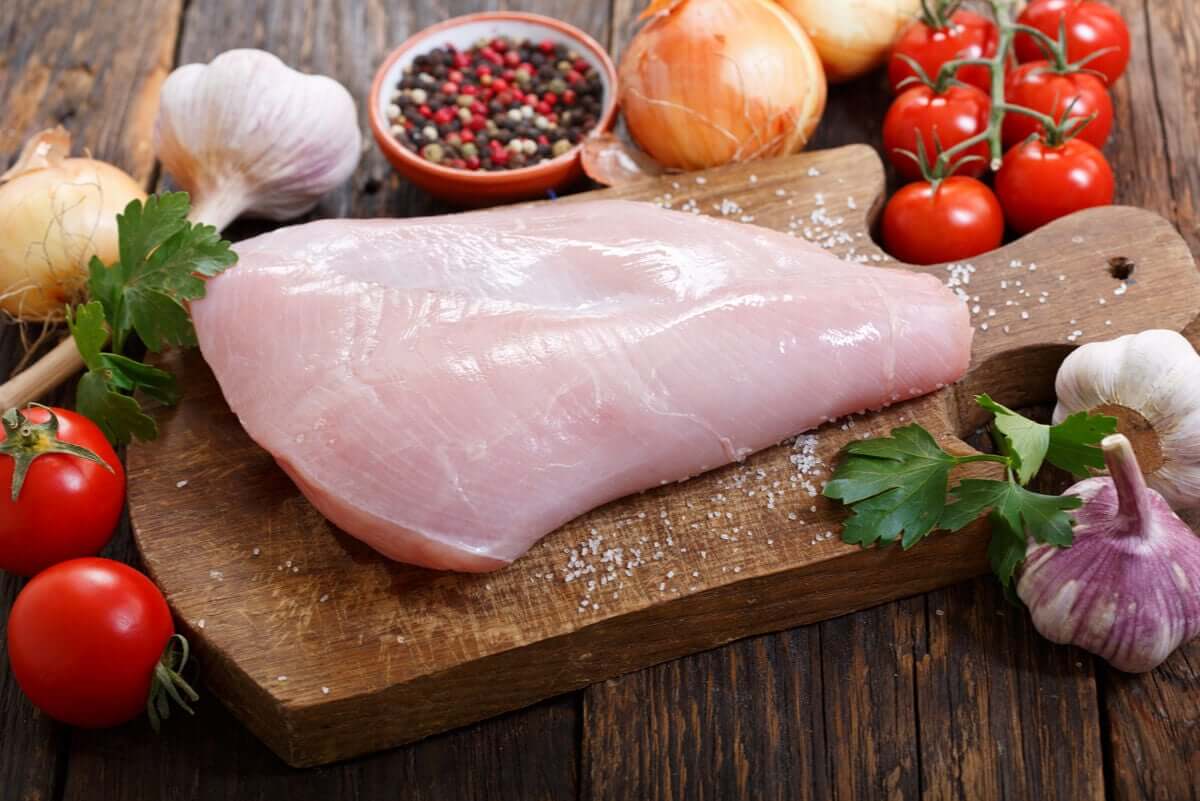Raw turkey on a cutting board with garlic, spices, tomatoes, and onion.