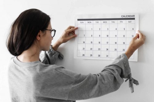 A woman putting up a calendar on the wall.