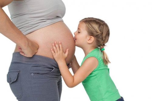 A girl kissing her mom's pregnant belly.