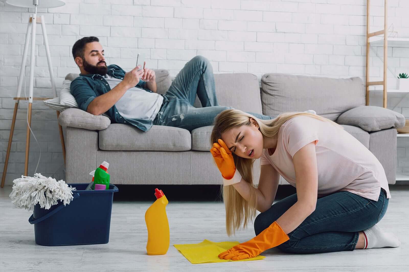 a woman looking angry as she cleans the floor and her husband relaxes on the couch.