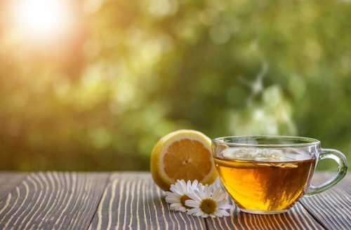 A cup of chamomile infusion with flowers and half a lemon on the side.
