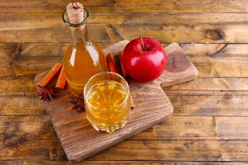 A wooden board with apple cider vinegar and an apple.