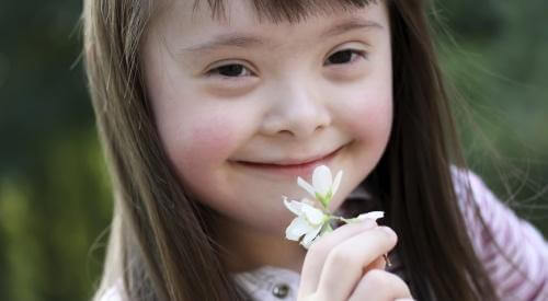 A girl with Down syndrome smelling a flower.