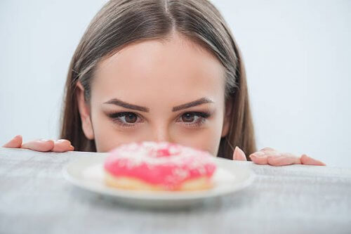 Woman staring at doughnut on table eating because of anxiety instant gratification