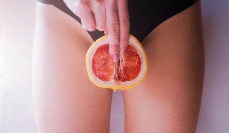 A woman with a grapefruit slice in front of her clitoris.