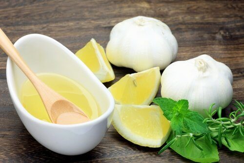 A bowl of garlic and lemon, two heads of garlic and some pieces of lemon and sprigs of mint and rosemary.