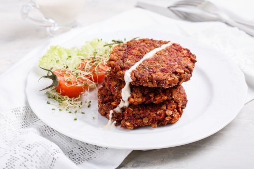 A serving of lentil-mushroom burgers with sprouts and tomato on the side.