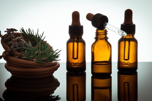 Three bottles of essential oils and a bowl with herbs.
