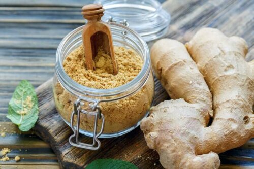 glass jar of ground ginger with whole ginger next to it on a wooden table