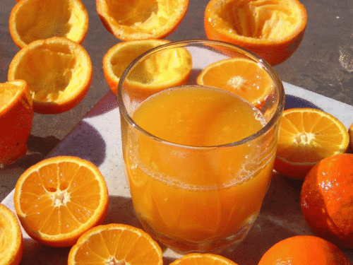 orange juice in a glass surrounded by fresh sliced oranges