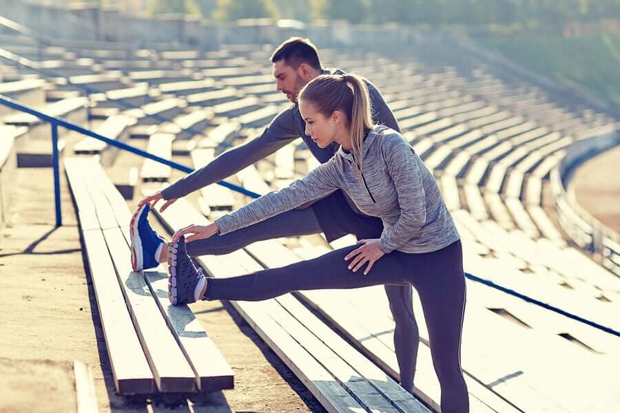 A man and a woman stretching their legs on bleachers.