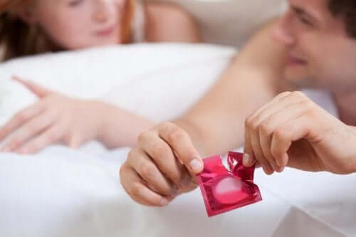 A couple in bed, the man is opening a condom.