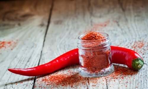 A little jar of cayenne pepper next to a pepper.