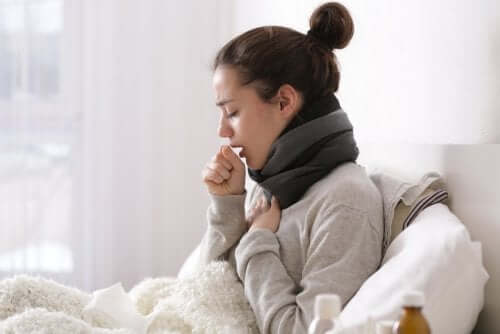 A woman in bed coughing trying to overcome a cold at home.
