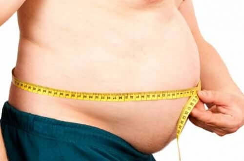 En mann med fedme som måler midjen.
