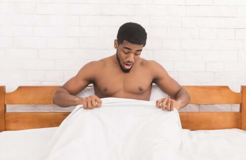 A surprised man looking under the sheets.