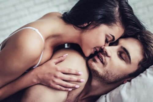Woman on top of man in bed about to kiss him.