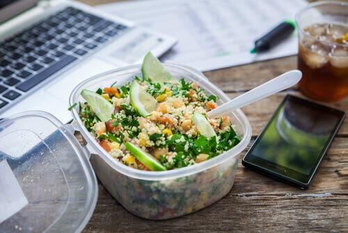Salad on desk next to phone and laptop.