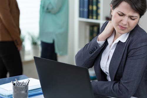 Kobieta siedząca, siedząca przed komputerem i cierpiąca na ból szyi.