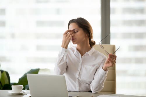 A woman using a laptop and rubbing her eyes.
