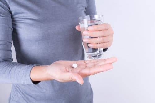Person with a glass of water and pain medication.