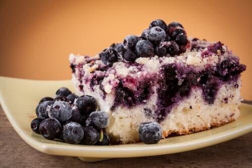 Blueberry cake on a plate with blueberries on top.